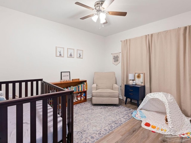 bedroom featuring ceiling fan, hardwood / wood-style floors, and a crib