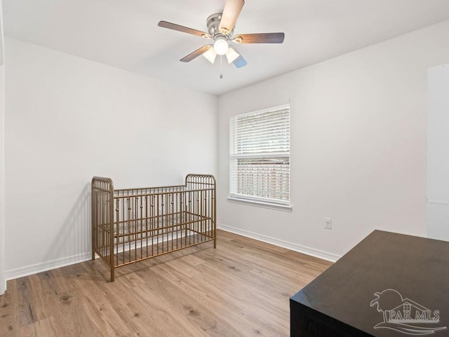 bedroom featuring ceiling fan, a nursery area, and light hardwood / wood-style floors