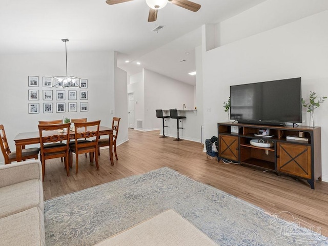 living room with ceiling fan with notable chandelier, lofted ceiling, and wood-type flooring