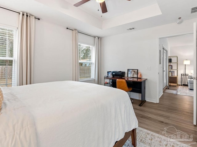 bedroom with ceiling fan, hardwood / wood-style flooring, and a tray ceiling