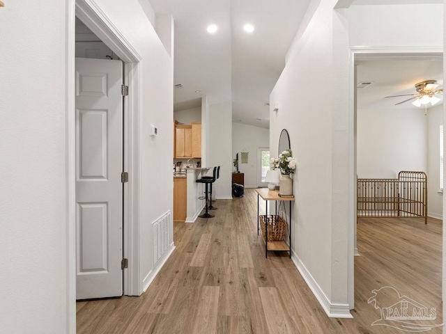 corridor with light hardwood / wood-style floors and lofted ceiling