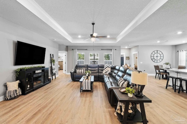 living area with ceiling fan, light wood-style flooring, plenty of natural light, a textured ceiling, and a tray ceiling