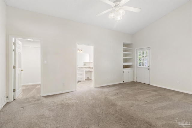 unfurnished bedroom with vaulted ceiling, connected bathroom, a spacious closet, ceiling fan, and light carpet