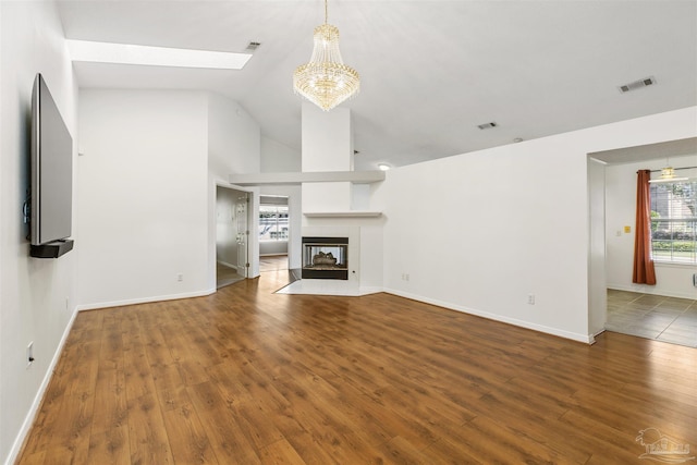 unfurnished living room featuring a multi sided fireplace, vaulted ceiling, wood-type flooring, and a notable chandelier