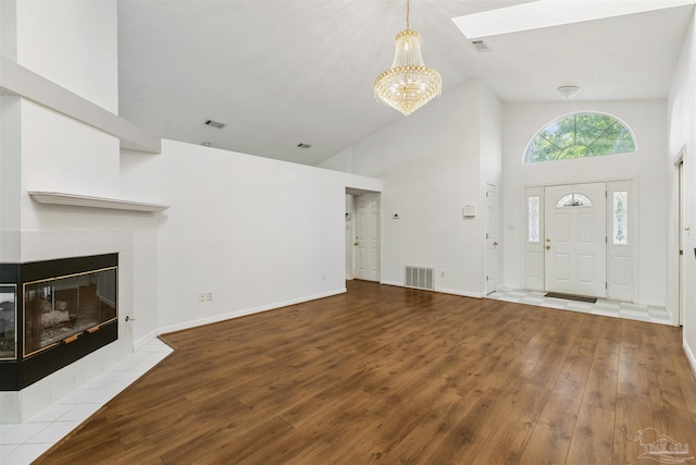 entrance foyer featuring wood-type flooring, a chandelier, a skylight, high vaulted ceiling, and a tile fireplace