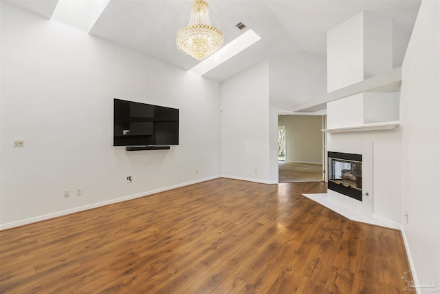 unfurnished living room with a tiled fireplace, a notable chandelier, hardwood / wood-style floors, and high vaulted ceiling