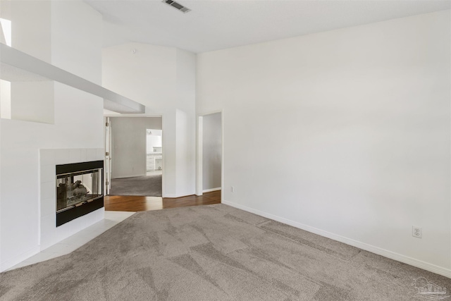 unfurnished living room featuring high vaulted ceiling, a tile fireplace, and light carpet