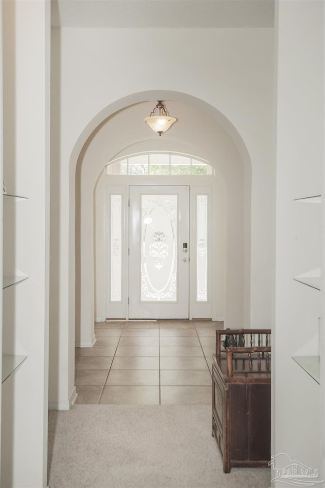 tiled foyer entrance featuring carpet flooring and arched walkways
