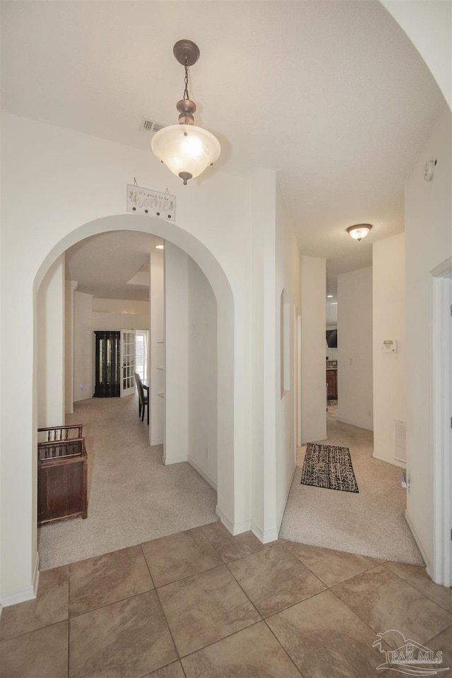hallway featuring visible vents, carpet flooring, and arched walkways