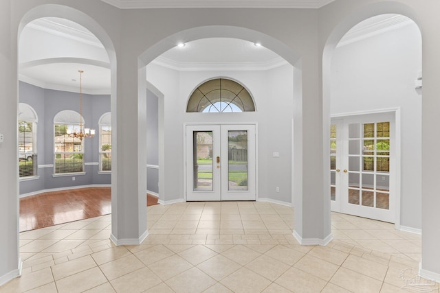 foyer featuring french doors, light tile patterned floors, crown molding, and a chandelier