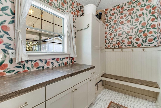 bathroom featuring wallpapered walls, tile patterned floors, a wainscoted wall, and a textured ceiling