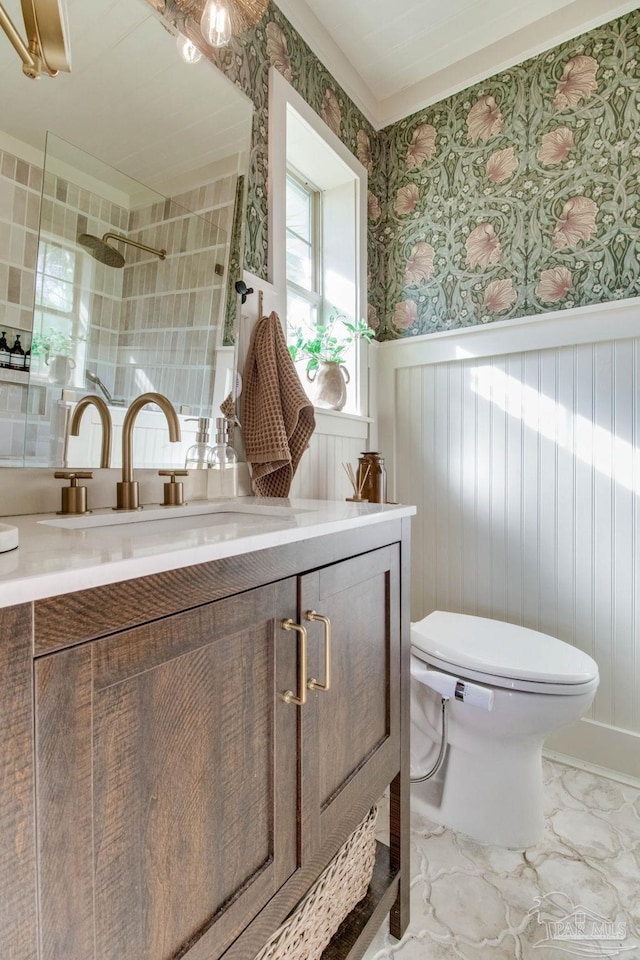 bathroom with a wainscoted wall, toilet, a tile shower, wallpapered walls, and vanity