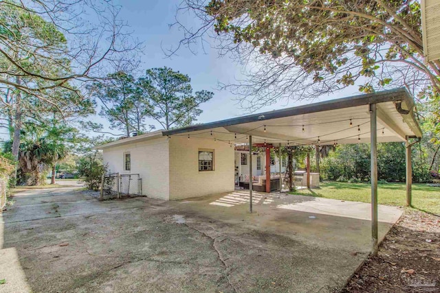 rear view of property with a patio, driveway, a carport, a lawn, and brick siding