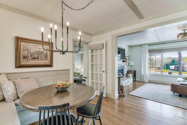 dining space featuring baseboards, a notable chandelier, a stone fireplace, and light wood finished floors