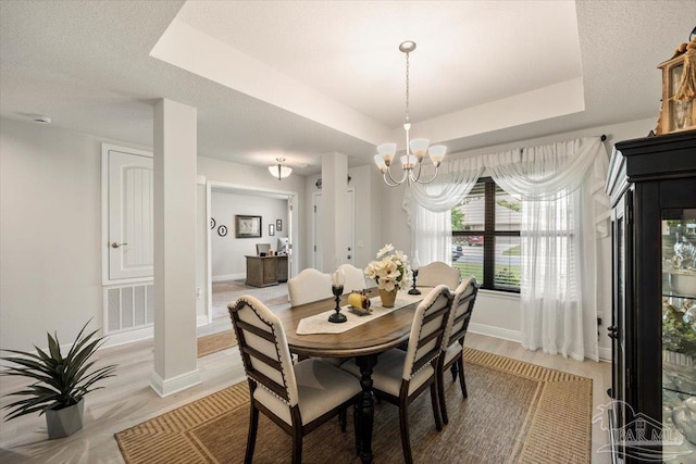 dining room featuring a tray ceiling, baseboards, light wood-style floors, and a chandelier