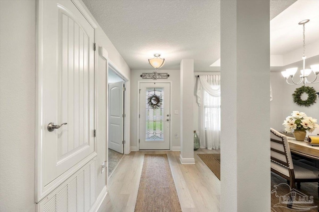 foyer entrance with light wood-style flooring, a chandelier, baseboards, and a textured ceiling