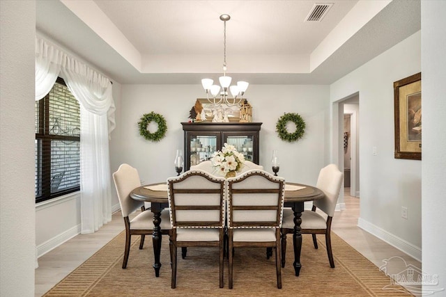 dining area with a chandelier, a tray ceiling, baseboards, and light wood-style flooring