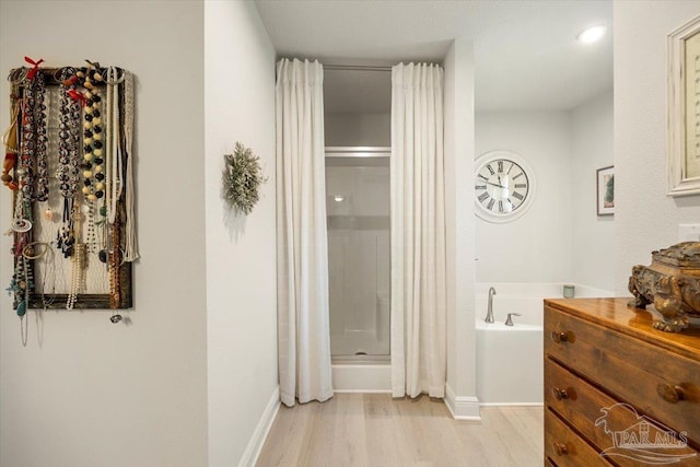 bathroom with wood finished floors, a shower stall, a bath, and baseboards