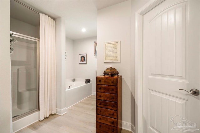 full bathroom featuring a stall shower, wood finished floors, a bath, baseboards, and recessed lighting