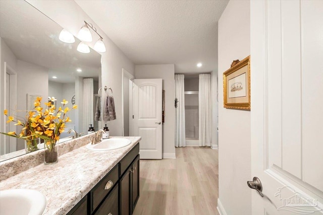 full bathroom featuring wood finished floors, double vanity, baseboards, and a textured ceiling