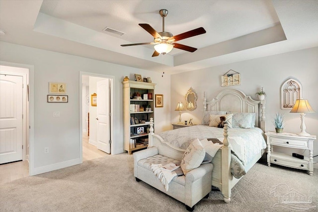 bedroom featuring a tray ceiling, light colored carpet, baseboards, a ceiling fan, and ensuite bathroom