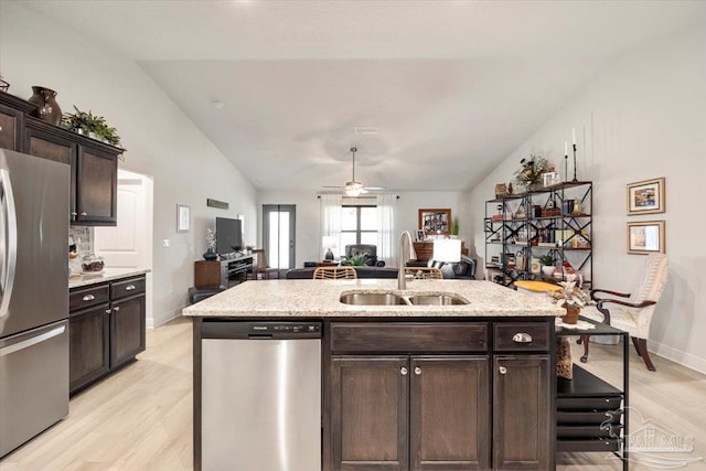 kitchen featuring appliances with stainless steel finishes, a sink, lofted ceiling, light wood-style floors, and open floor plan
