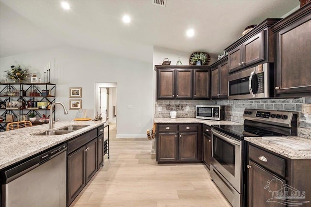 kitchen with stainless steel appliances, a sink, lofted ceiling, dark brown cabinets, and tasteful backsplash