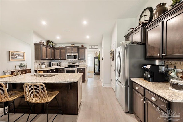 kitchen featuring a sink, appliances with stainless steel finishes, dark brown cabinets, backsplash, and a breakfast bar area