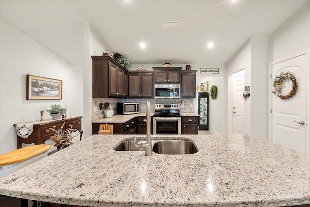 kitchen with stainless steel appliances, a sink, dark brown cabinetry, a large island, and decorative backsplash