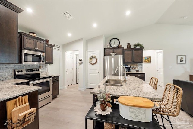 kitchen featuring appliances with stainless steel finishes, a sink, lofted ceiling, backsplash, and dark brown cabinetry