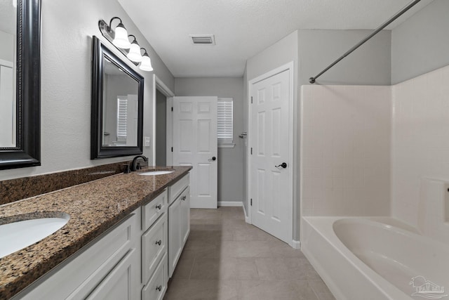 bathroom with a textured ceiling, bathing tub / shower combination, tile patterned flooring, and vanity