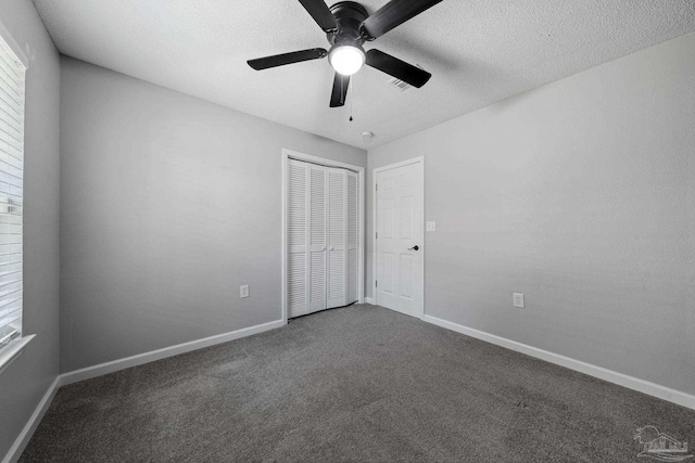 unfurnished bedroom with a closet, dark colored carpet, ceiling fan, and a textured ceiling