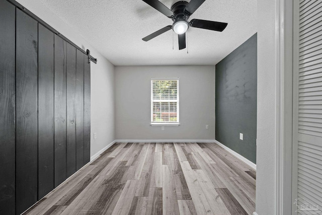 unfurnished bedroom featuring a barn door, a textured ceiling, light hardwood / wood-style floors, and ceiling fan