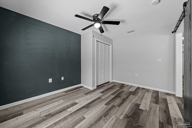 unfurnished bedroom with ceiling fan, wood-type flooring, a textured ceiling, a closet, and a barn door