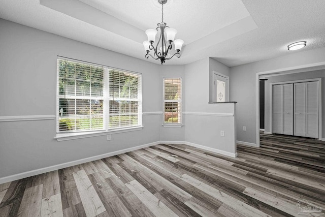 unfurnished dining area featuring an inviting chandelier, a raised ceiling, a textured ceiling, and dark hardwood / wood-style flooring