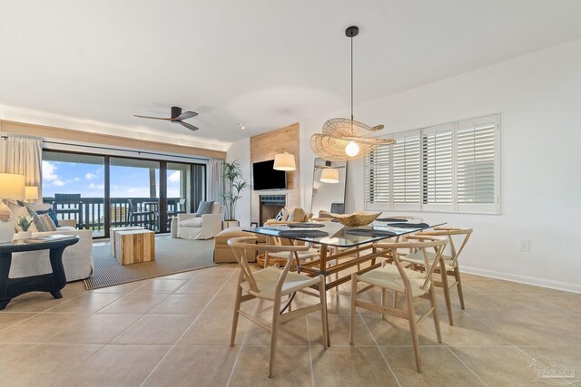 dining space with light tile patterned floors, ceiling fan, a fireplace, and baseboards