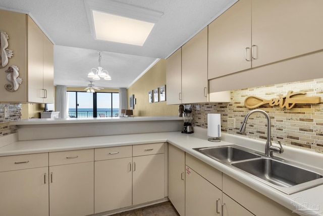 kitchen with ceiling fan, decorative backsplash, hanging light fixtures, a water view, and sink