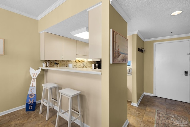 kitchen with a textured ceiling, crown molding, a breakfast bar area, and tasteful backsplash