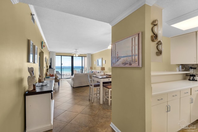 interior space featuring ceiling fan, a textured ceiling, crown molding, and a water view