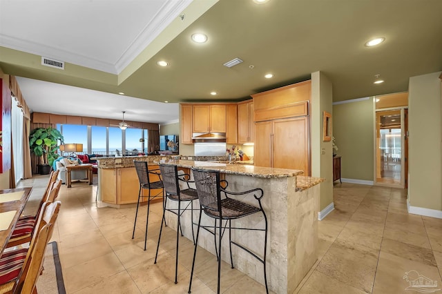 kitchen featuring a breakfast bar area, crown molding, a center island, light brown cabinets, and light stone countertops
