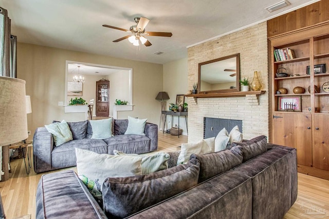 living room featuring a brick fireplace, ceiling fan with notable chandelier, and light wood-type flooring