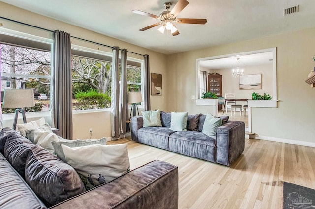 living room featuring ceiling fan with notable chandelier and light hardwood / wood-style flooring