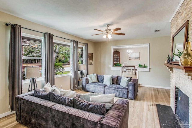 living room featuring a fireplace, ceiling fan with notable chandelier, and light hardwood / wood-style flooring