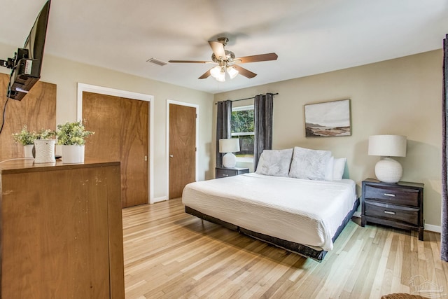 bedroom with ceiling fan, light hardwood / wood-style flooring, and two closets