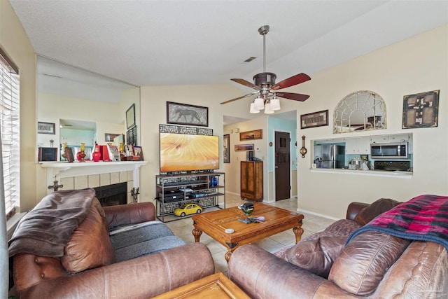 living room featuring a tiled fireplace, lofted ceiling, ceiling fan, and light tile patterned flooring