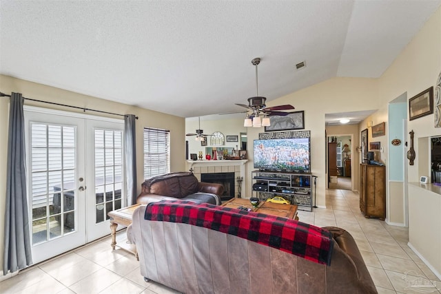 tiled living room featuring a tile fireplace, lofted ceiling, ceiling fan, a textured ceiling, and french doors