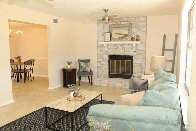 living room with a stone fireplace and ceiling fan with notable chandelier