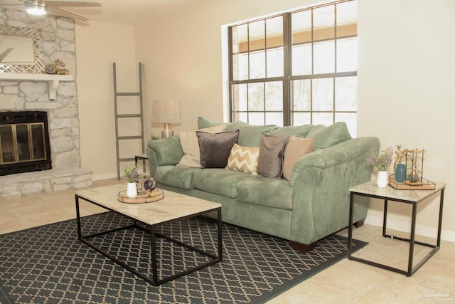 tiled living room featuring ceiling fan and a stone fireplace