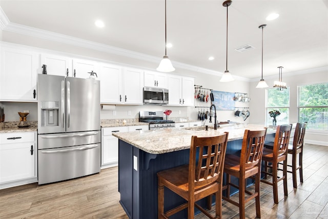 kitchen featuring white cabinets, decorative light fixtures, stainless steel appliances, and a kitchen island with sink