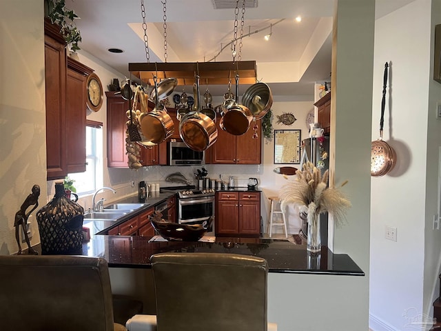 kitchen featuring sink, stainless steel appliances, decorative backsplash, kitchen peninsula, and dark stone counters